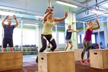 fitness, sport, training and exercising concept - group of people doing box jumps in gym. group of people doing box jumps exercise in gym