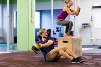 fitness, sport, training, exercising and people concept - woman and man with medicine ball doing curl ups and box jumps in gym. woman and man with medicine ball exercising in gym