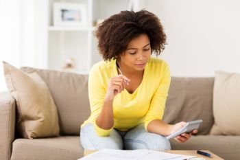 budget, finances and people concept - african american woman with papers and calculator counting money at home. african woman with papers and calculator at home