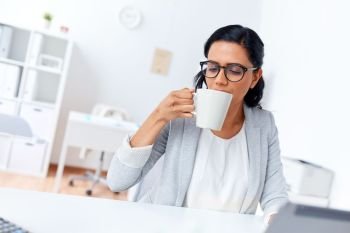 business, break and people concept - smiling businesswoman drinking coffee or tea at office. businesswoman drinking coffee or tea at office