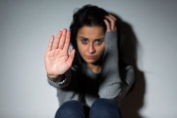 people and domestic violence concept - unhappy crying woman sitting on floor and showing defensive gesture. unhappy crying woman showing defensive gesture