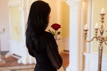 burial, people and mourning concept - sad woman with red rose at funeral in church. sad woman with red rose at funeral in church