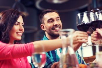 leisure, celebration, drinks, people and holidays concept - happy couple and friends clinking glasses of wine at restaurant. friends clinking glasses of wine at restaurant