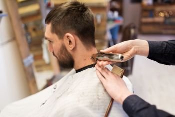 grooming, hairstyle and people concept - man and barber or hairdresser hands with trimmer cutting hair at barbershop. man and barber hands with trimmer cutting hair