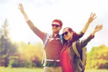 travel, hiking, backpacking, tourism and people concept - happy couple with backpacks waving hands and walking along country road outdoors. happy couple with backpacks hiking outdoors