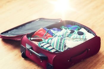 summer vacation, travel, tourism and objects concept - close up of travel bag with beach clothes, sunglasses and sunscreen. close up of travel bag with beach clothes