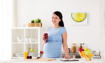 pregnancy, people and healthy eating concept - happy smiling pregnant woman drinking juice or smoothie at home kitchen. happy pregnant woman drinking juice at home