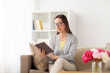 literature, education and people concept - young woman in glasses reading book at home. young woman in glasses reading book at home