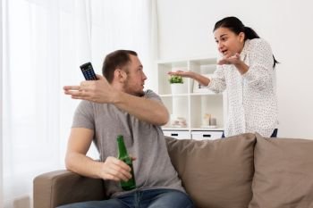 people, relationship difficulties, conflict and family concept - angry woman having argument with man drinking beer and watching tv at home. couple having argument at home