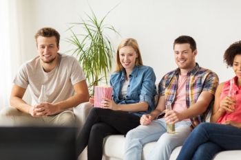 friendship, junk food, people and entertainment concept - happy friends with popcorn and beer watching tv at home. happy friends with popcorn watching tv at home
