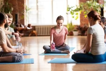 fitness, sport and healthy lifestyle concept - group of people with water bottles in yoga class resting on mats at studio. group of people resting on yoga mats at studio