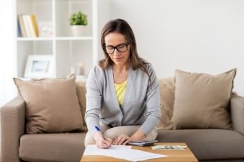 business, savings, finances and people concept - woman with money, papers and calculator at home. woman with money, papers and calculator at home