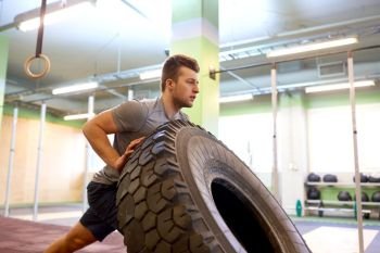 strongman, bodybuilding, sport, fitness and people concept - young man doing tire flip at training in gym. man doing strongman tire flip training in gym