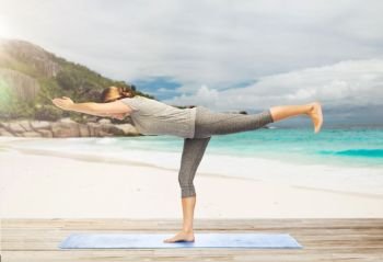 fitness, people and healthy lifestyle concept - woman doing yoga warrior pose on half-bent right leg on mat over exotic tropical beach background. woman doing yoga warrior pose on half-bent outdoor