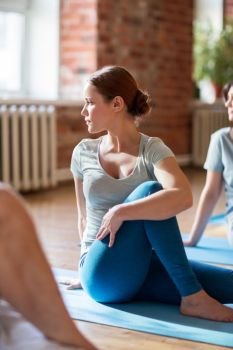 fitness, sport and healthy lifestyle concept - woman with group of people doing yoga seated spinal twist pose in gym or studio. woman with group of people doing yoga at studio