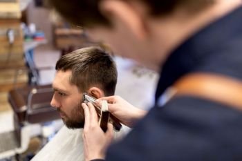 grooming, hairstyle and people concept - man and barber or hairdresser hands with trimmer cutting hair at barbershop. man and barber hands with trimmer cutting hair