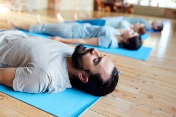 fitness, sport and healthy lifestyle concept - group of people doing yoga corpse pose on mats at studio. man with group of people doing yoga at studio