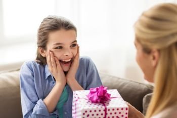 people, holidays and family concept - happy girl receiving birthday present from mother at home. mother giving birthday present to girl at home