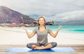 fitness, people and healthy lifestyle concept - woman doing yoga meditation in lotus pose on mat over exotic tropical beach background. woman doing yoga meditation in lotus pose on beach