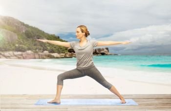 fitness, sport and people concept - woman doing yoga warrior pose on mat over exotic tropical beach background. woman doing yoga warrior pose on beach