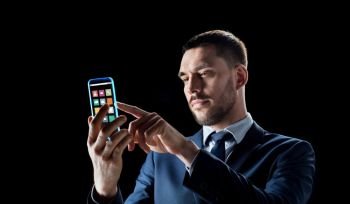 business, multimedia and future technology concept - businessman working with media icons on transparent smartphone screen over black background. businessman with transparent smartphone