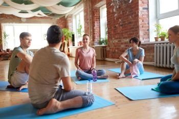 fitness, sport and healthy lifestyle concept - group of people with water bottles and towels in yoga class resting on mats at studio. group of people resting on yoga mats at studio