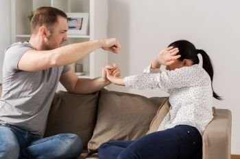 domestic violence, abuse and people concept - couple having fight and man beating helpless woman at home. unhappy woman suffering from home violence