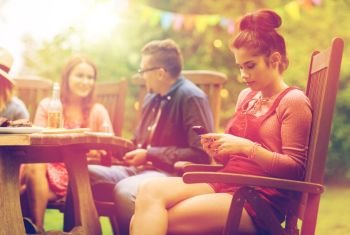 leisure, holidays, people and technology concept - young woman or teenage girl texting on smartphone and friends having dinner at summer garden party. woman with smartphone and friends at summer party