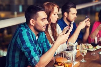 leisure, technology, lifestyle and people concept - happy friends with smartphones dining at restaurant. friends with smartphones dining at restaurant