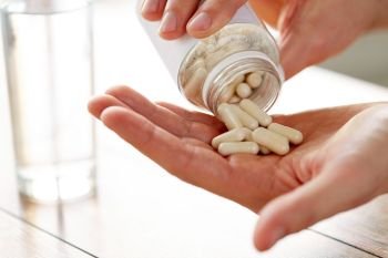 healthcare, medicine, nutritional supplements and people concept - close up of man pouring pills from jar to hand. close up of man pouring pills from jar to hand