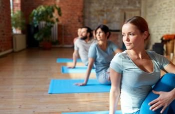 fitness, sport and healthy lifestyle concept - group of people doing yoga seated spinal twist pose in gym or studio. group of people doing yoga exercises at studio