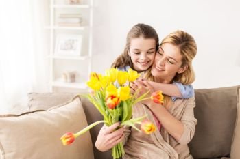 people, family and holidays concept - happy girl giving tulip flowers and hugging her mother at home. happy girl giving flowers to mother at home