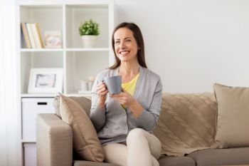 people, drinks and leisure concept - happy woman with mug drinking tea or coffee at home. happy woman drinking tea or coffee at home