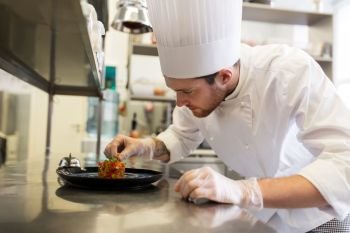 food cooking, profession and people concept - happy male chef cook serving and garnishing stewed vegetables on plate at restaurant kitchen. happy male chef cooking food at restaurant kitchen