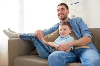 family, childhood, fatherhood and people concept - happy father and little son sitting on sofa at home. happy father and son sitting on sofa at home
