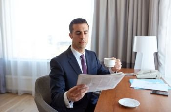 business trip, people and mass media concept - businessman reading newspaper and drinking coffee at hotel room. businessman reading newspaper and drinking coffee