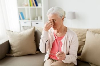 old age, health problem, vision and people concept - senior woman with glasses sitting on sofa and having headache at home. senior woman with glasses having headache at home