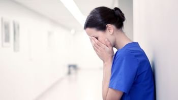 people, medicine, healthcare and sorrow concept - sad or crying female nurse at hospital corridor. sad or crying female nurse at hospital corridor
