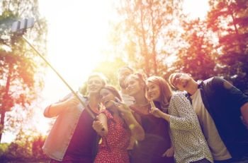 leisure, party, technology, people and holidays concept - happy friends taking picture with smartphone selfie stick at summer garden. friends taking selfie at party in summer garden