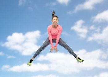 sport, fitness, motion and people concept - happy smiling young woman jumping in air over blue sky and clouds background. happy smiling sporty young woman jumping in sky