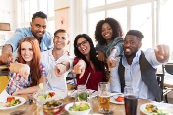 leisure, food and people concept - group of happy international friends eating at restaurant ant pointing finger at you table. happy friends eating at restaurant