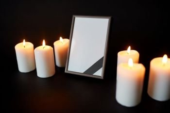 funeral and mourning concept - empty photo frame with ribbon and burning candles over black background. black ribbon on photo frame and candles at funeral