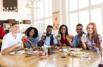 leisure, food and people concept - group of happy international friends with drinks eating at restaurant table. happy friends eating and drinking at restaurant