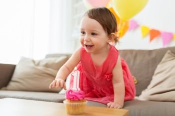 childhood, people and celebration concept - happy baby girl with cupcake on birthday party at home. baby girl with birthday cupcake at home party