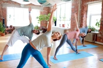 fitness, sport and healthy lifestyle concept - group of people doing yoga in triangle pose at studio. group of people doing yoga triangle pose at studio