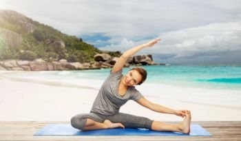 fitness, sport and people concept - happy woman doing yoga and stretching on mat over exotic tropical beach background. happy woman doing yoga and stretching on beach