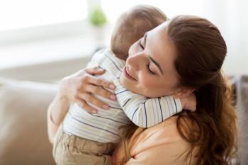 family, child and motherhood concept - happy smiling young mother hugging little baby at home. happy young mother hugging little baby at home