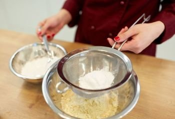 cooking food, baking and people concept - chef with strainer sieving flour into bowl and making batter or dough. chef with flour in bowl making batter or dough
