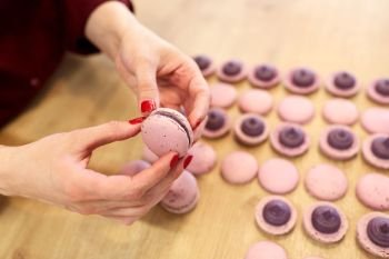 cooking, confectionery and food concept - chef sandwiching baked macarons shells with cream together at pastry shop. chef sandwiching macarons shells with cream