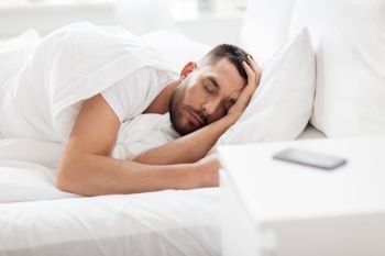 people, bedtime and rest concept - man sleeping in bed at home with smartphone on nightstand. man sleeping in bed with smartphone on nightstand